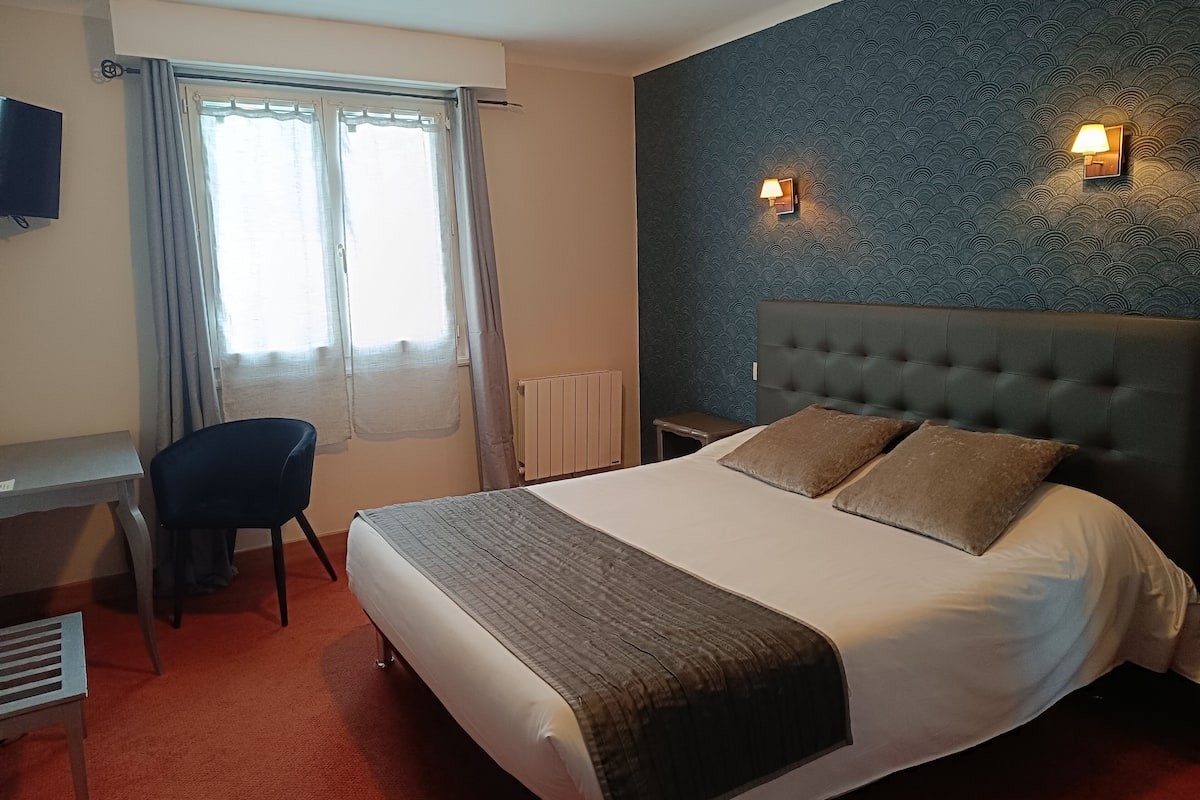 A hotel room with a bed, a desk, a chair, and a window with curtains.
