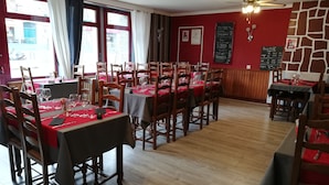 Un restaurante con mesas y sillas de madera, manteles rojos y una pared de piedra.