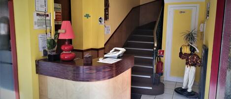 A hotel reception area with a curved desk, a telephone, a red lamp, and a staircase leading to another floor.