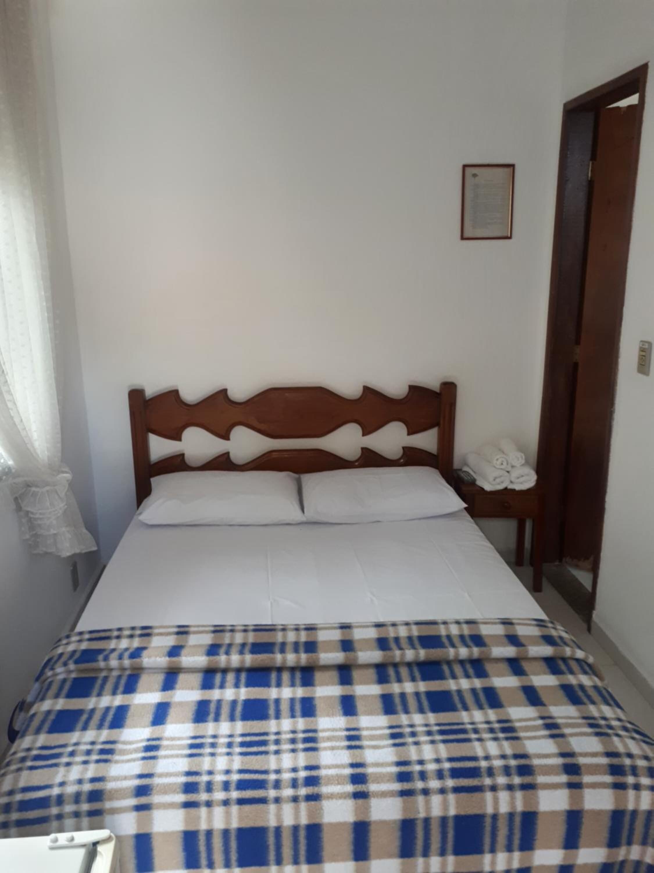 A bed with a plaid blanket, a wooden headboard, and a bedside table with towels.