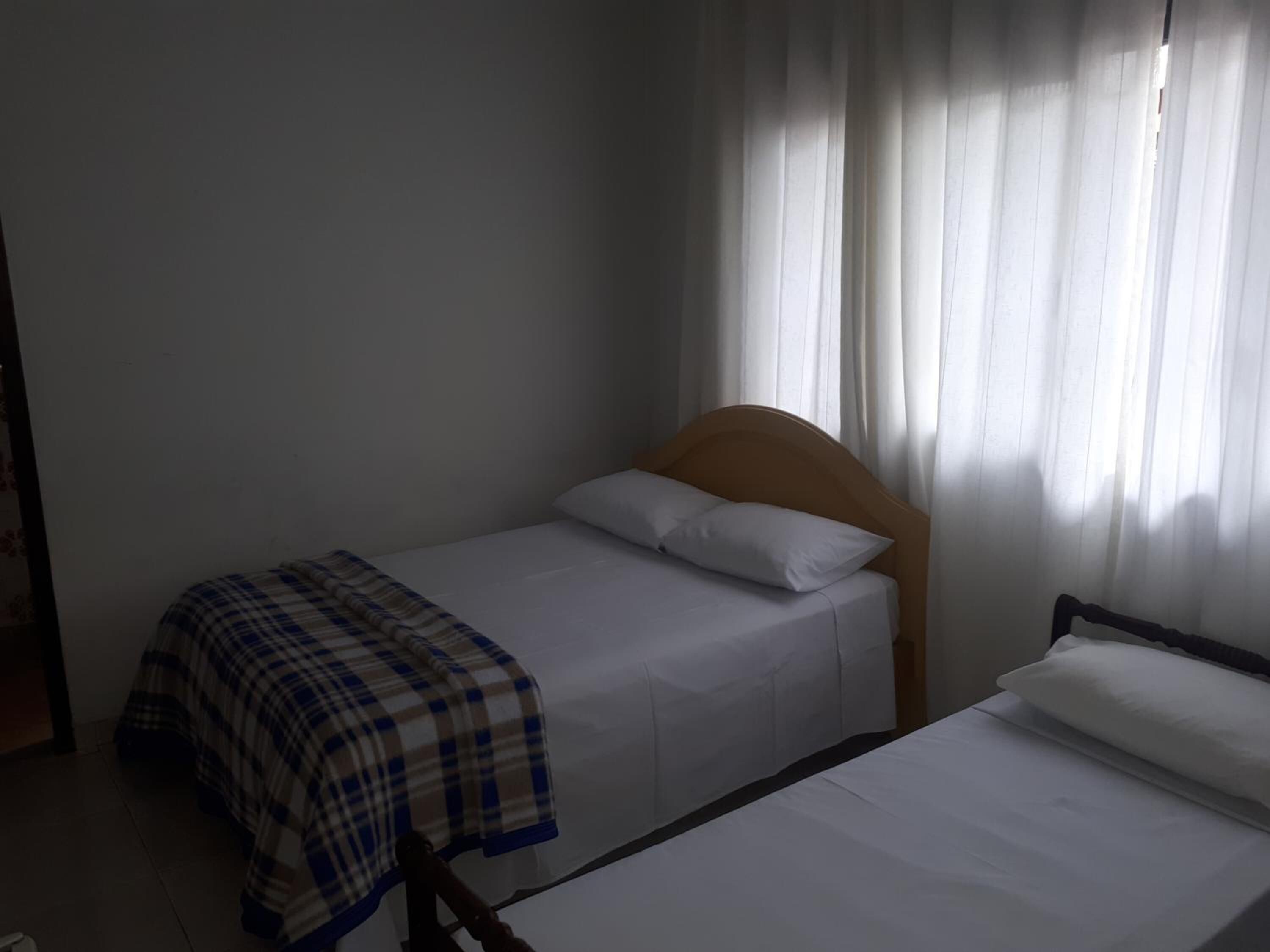 A single bed with a wooden headboard, a plaid blanket, and white bedding.