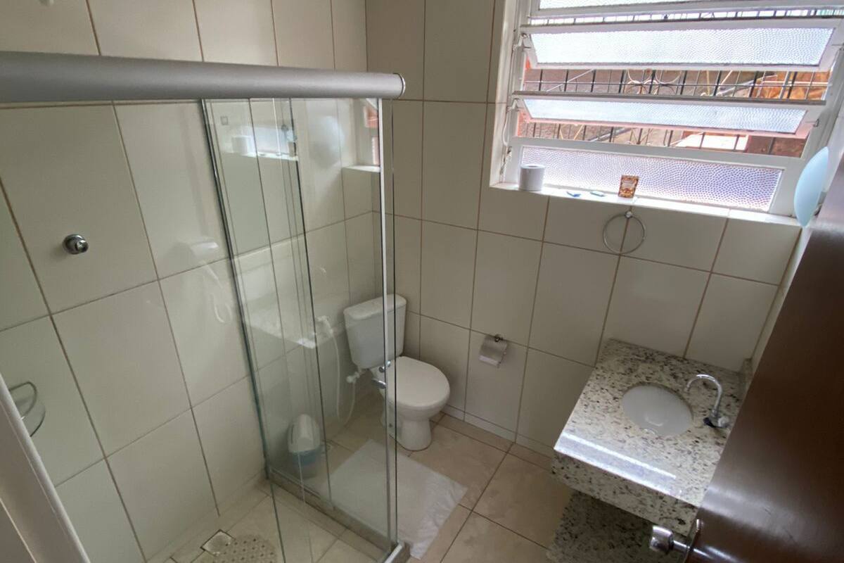 Ein Badezimmer mit Duschkabine aus Glas, Toilette, Waschbecken mit Granitplatte und Fenster mit Blick nach draußen.