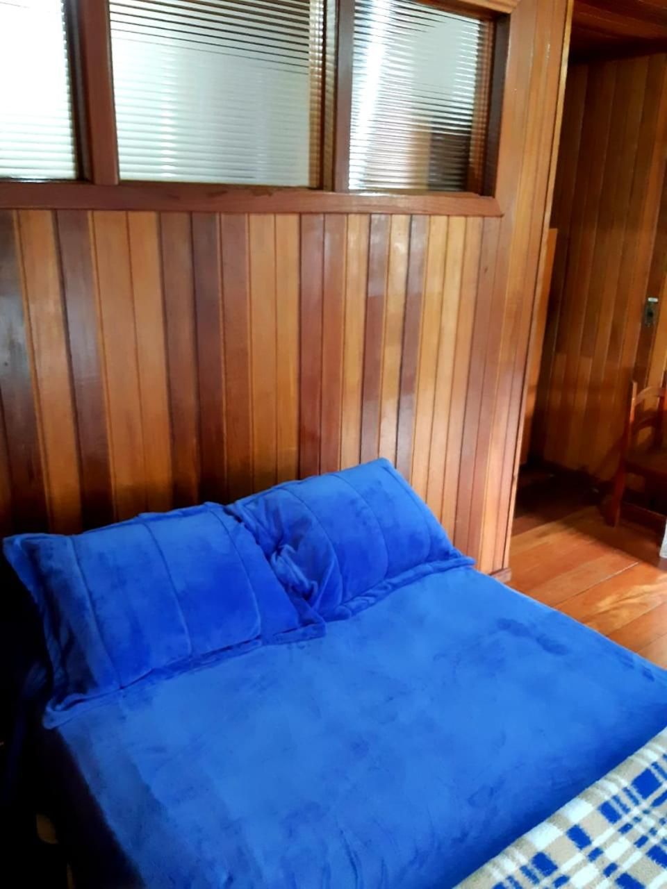 A room with a bed, wooden paneling, and a window with blinds.