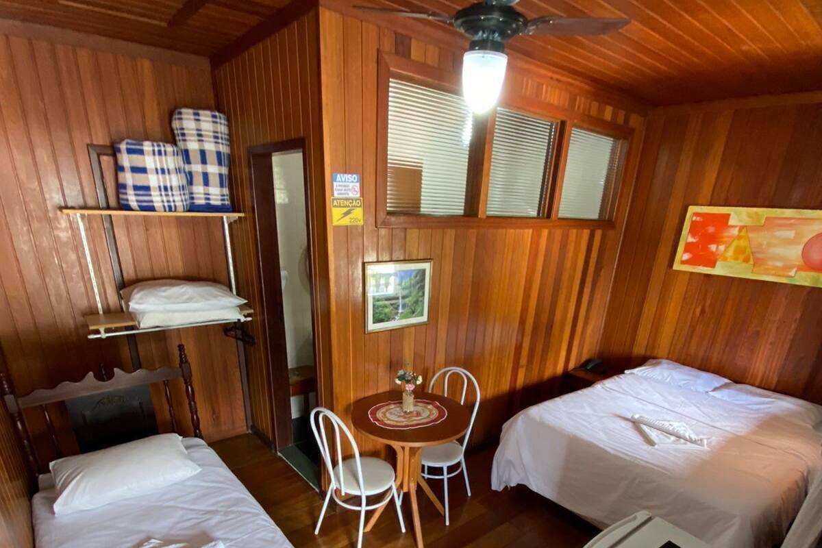 Ein Zimmer mit zwei Betten, einem kleinen Tisch mit Stühlen, einem Deckenventilator und einem an der Wand befestigten Fernseher.