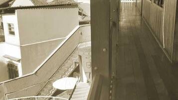 A corridor with a wooden floor, a white wall on the left, and a building with a tiled roof in the background.