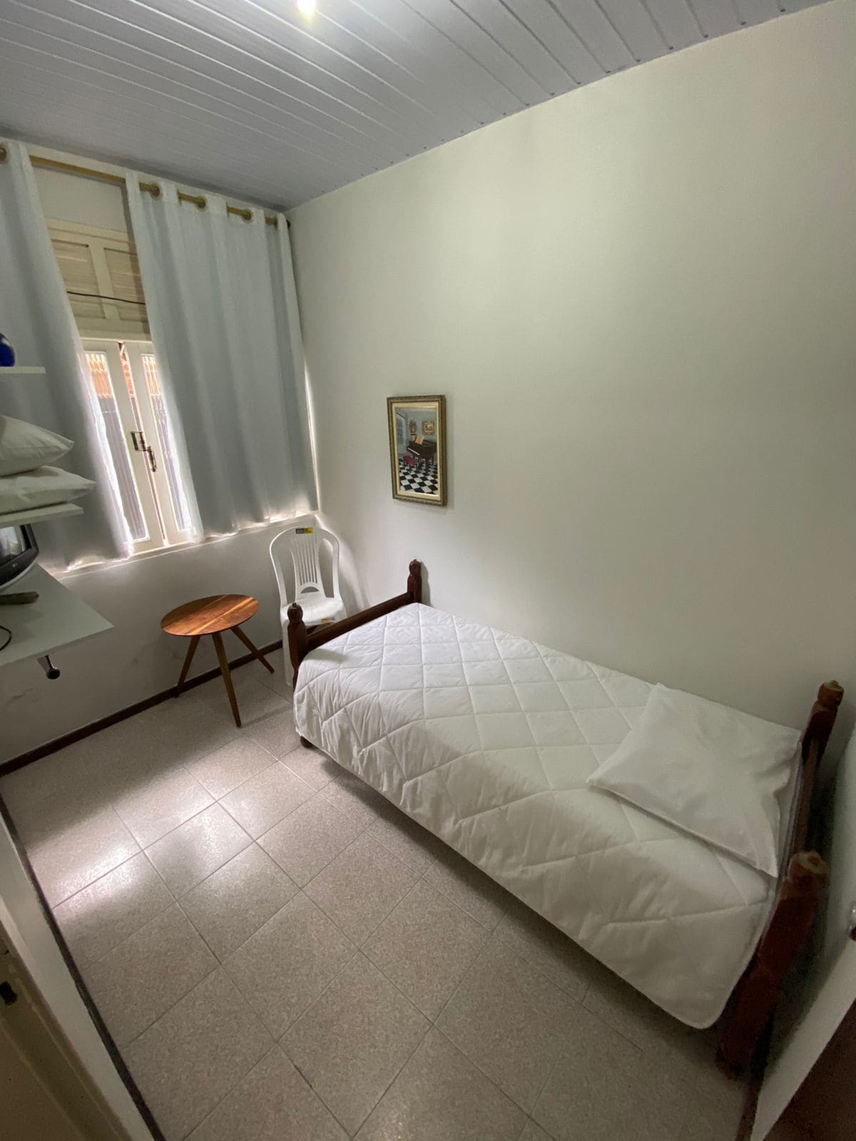 Une petite pièce propre, avec un lit simple, une chaise et une table.