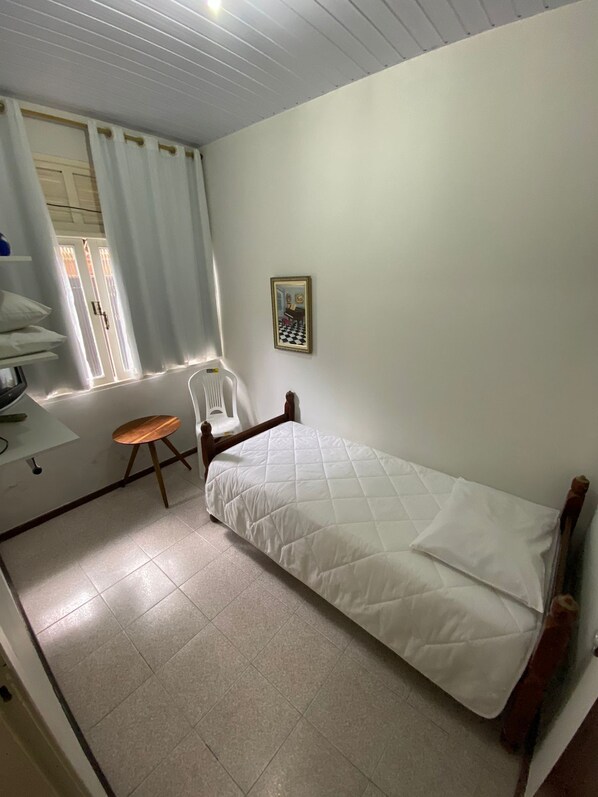 Una habitación pequeña y limpia con una cama individual, una silla y una mesa.