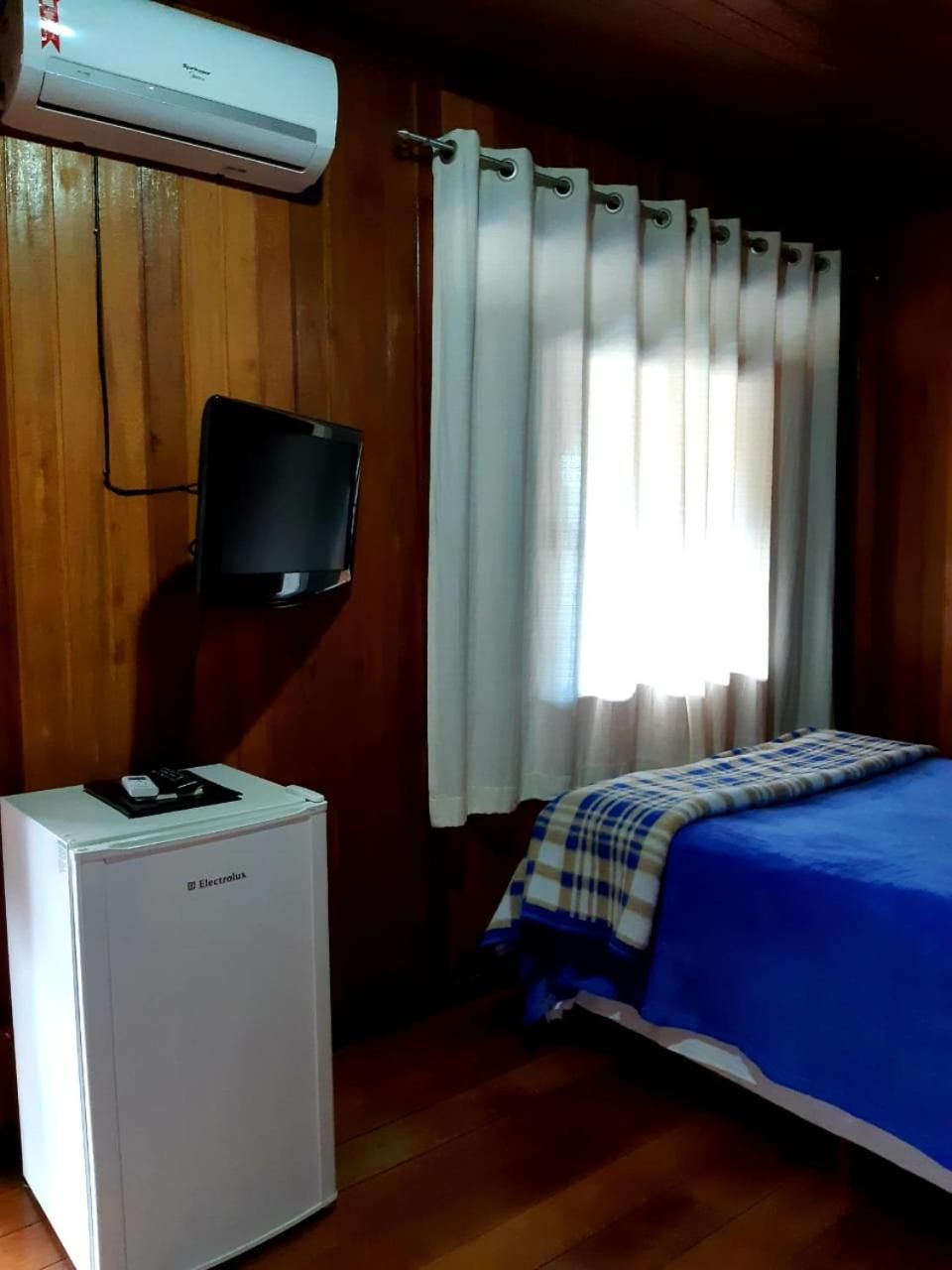 A room with a bed, a television mounted on the wall, and a white refrigerator.