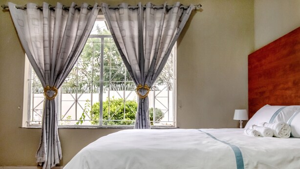 A hotel room with a large bed, a window with curtains, and a view of greenery outside.