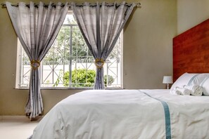 Una habitación de hotel con una cama grande, una ventana con cortinas y vistas a la vegetación.