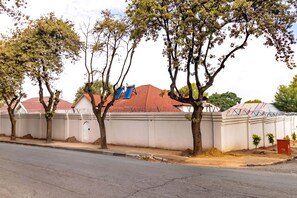 Vista de la calle con un muro blanco, árboles y un edificio con techo rojo.