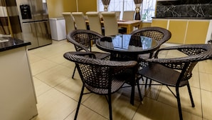 A kitchen with a round table, wicker chairs, a refrigerator, and a television on the wall.