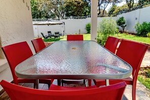 Una mesa con superficie de vidrio y sillas rojas en un patio al aire libre.