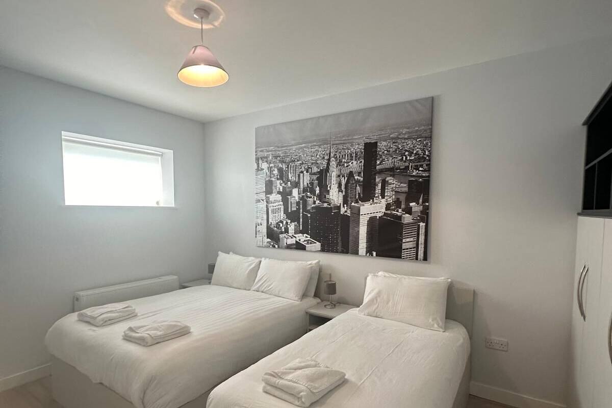 A modern bedroom with two beds, a cityscape artwork, a ceiling light, and a window.