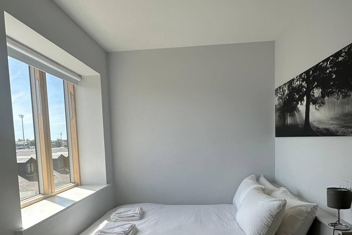 A modern bedroom with a single bed, a window with blinds, a nightstand, and a wall-mounted lamp.
