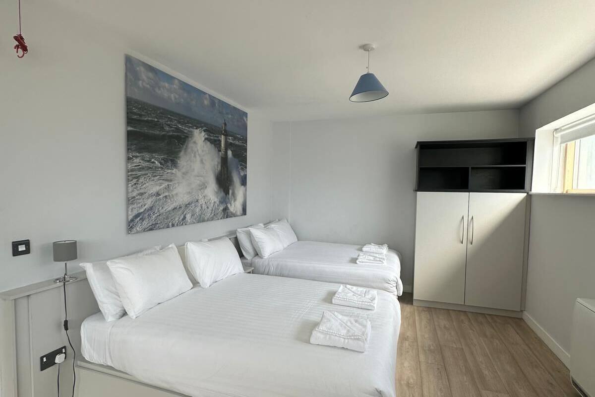 A modern bedroom with a large bed, a side table, a lamp, a painting of a ship, and a wardrobe.