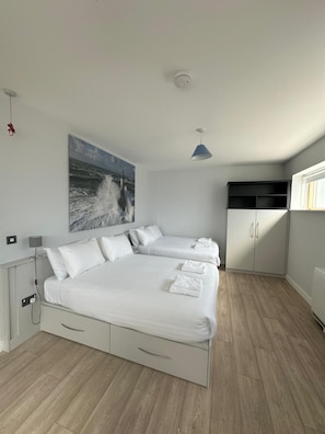 A modern bedroom with a large bed, a side table, a lamp, a painting of a ship, and a wardrobe.