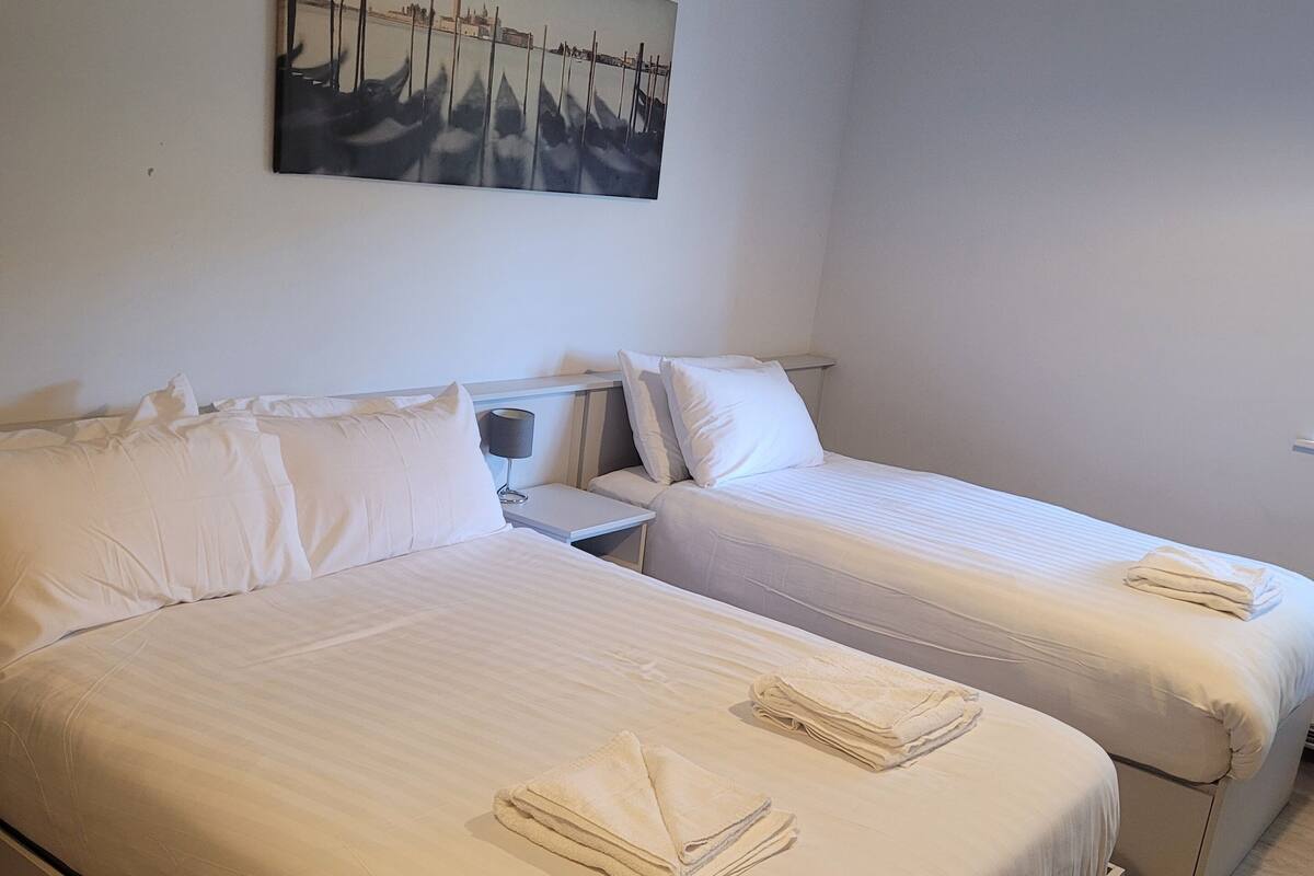 A hotel room with two beds, a nightstand, a lamp, and a painting on the wall.
