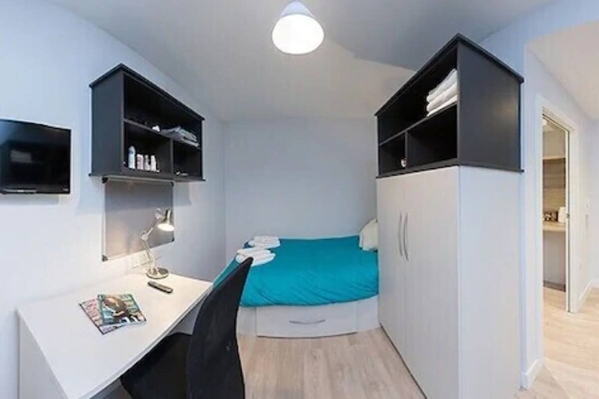 A compact bedroom with a bed, a desk, and built-in shelving.