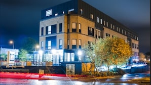 Un edificio moderno de varios pisos con tejado plano, ventanas amplias y un cartel visible en la parte superior.