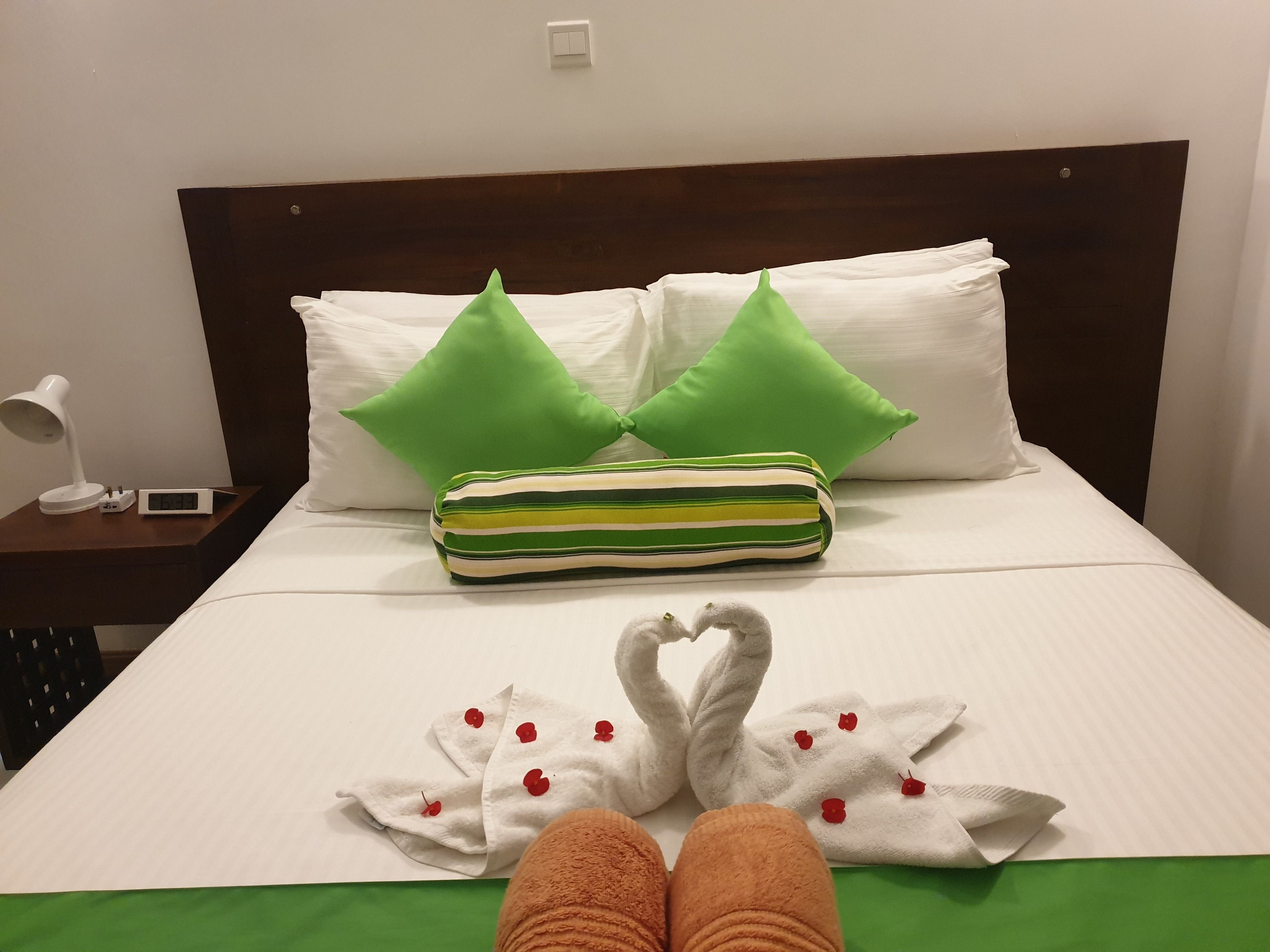 Un lit bien fait, agrémenté d’oreillers verts, d’un coussin rayé et d’une serviette ornée de cerises rouges.