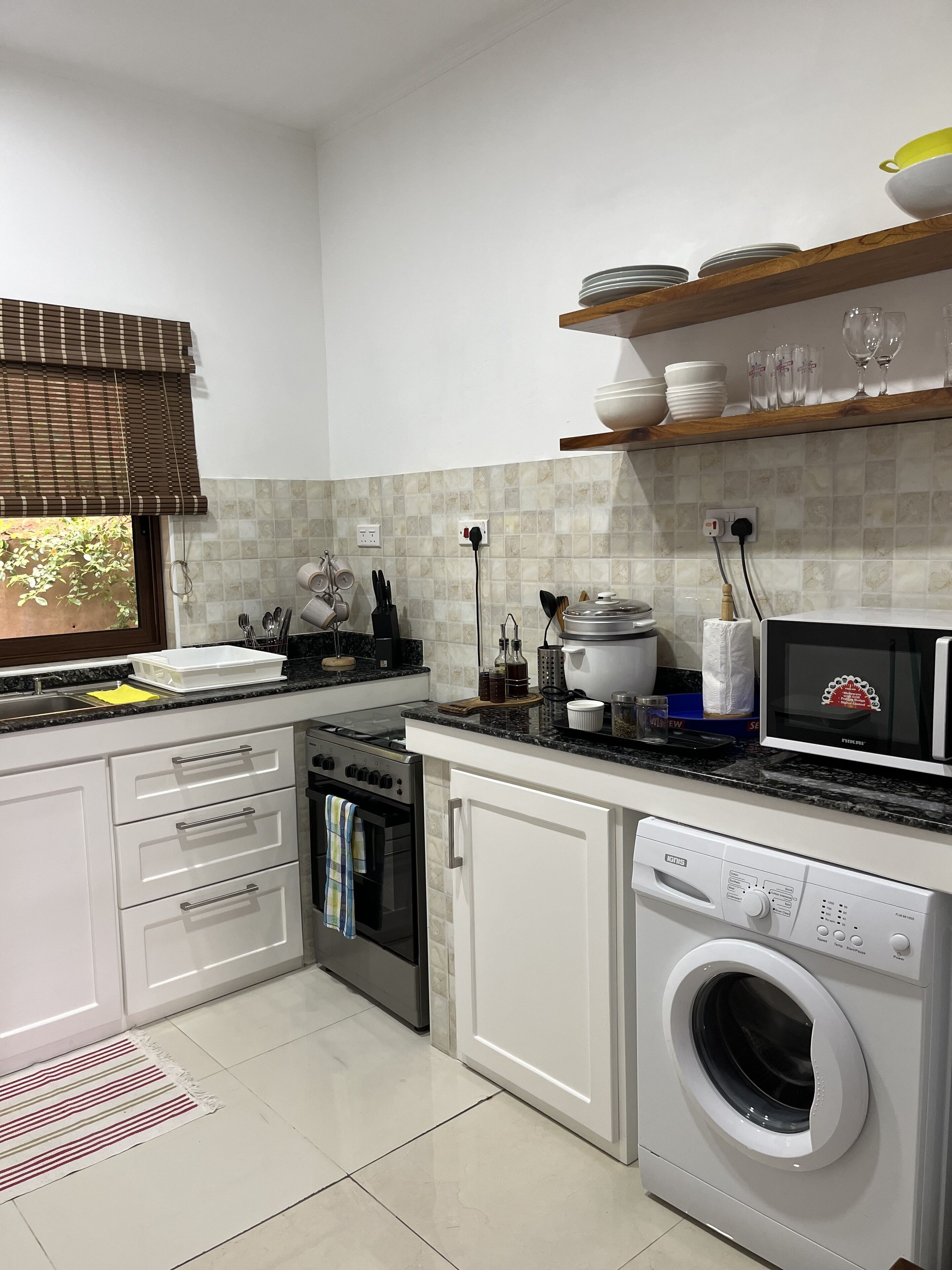 A modern kitchen with white cabinets, a built-in oven, a microwave, and a washing machine.