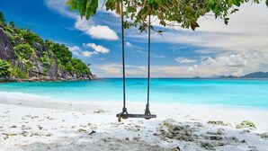 Ein Strand mit Schaukeln, klarem türkisblauem Wasser und felsigen Klippen.