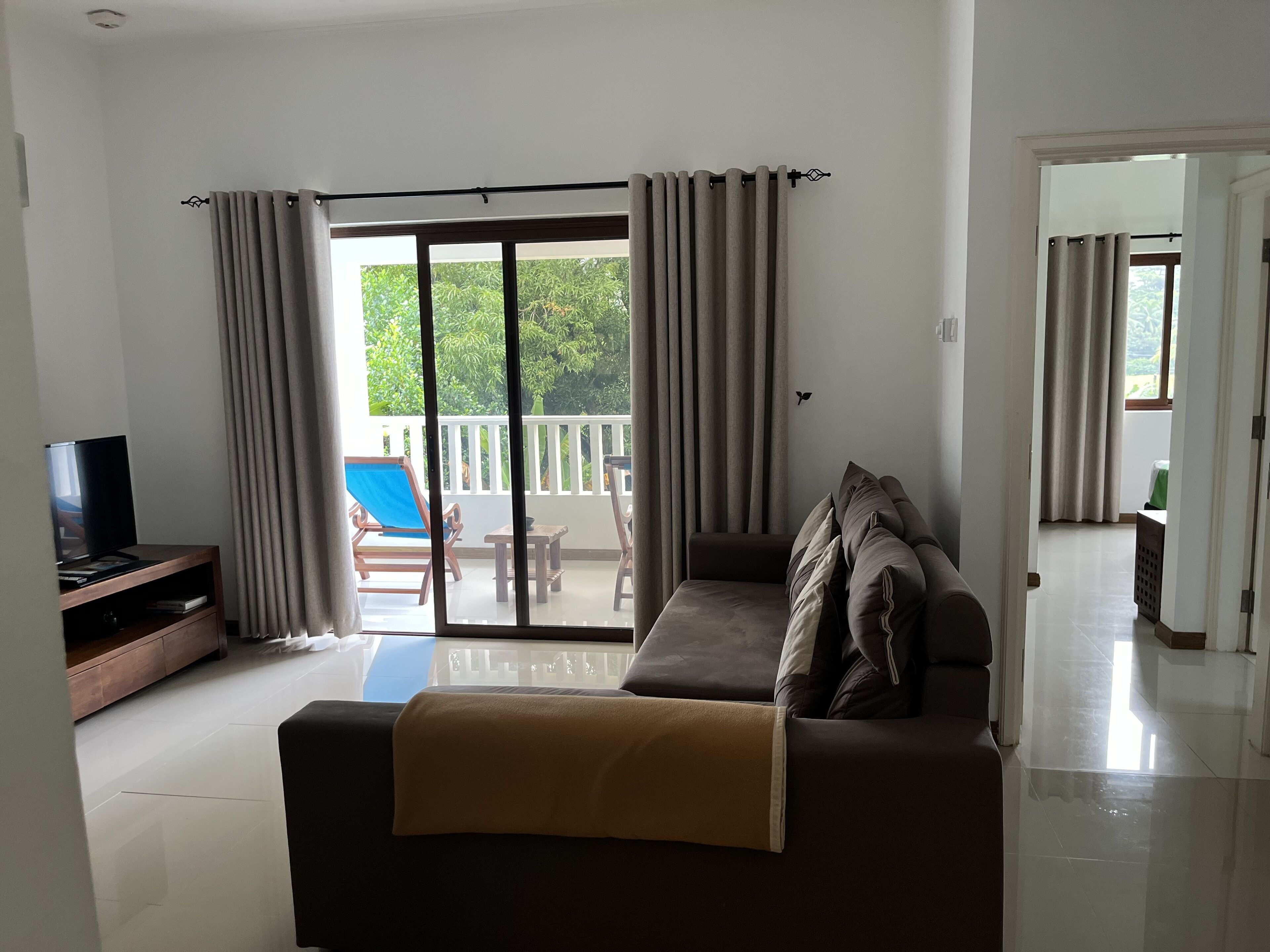 A living room with a sofa, a TV, and a balcony with curtains.