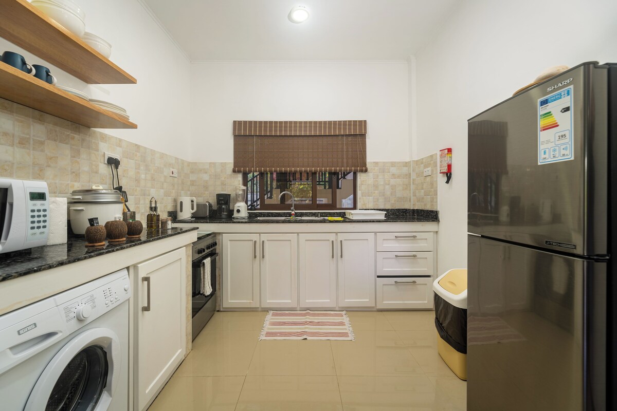 A compact kitchen with white cabinets, a stainless steel refrigerator, a washing machine, and a microwave.