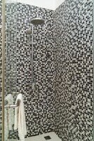 Ducha con pared de azulejos a cuadros, cabezal de ducha de mano y toallero con una toalla.