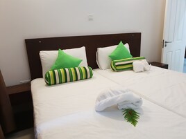 Una cama bien hecha con ropa blanca, almohadas a rayas verdes y una toalla blanca con un adorno de hoja verde.