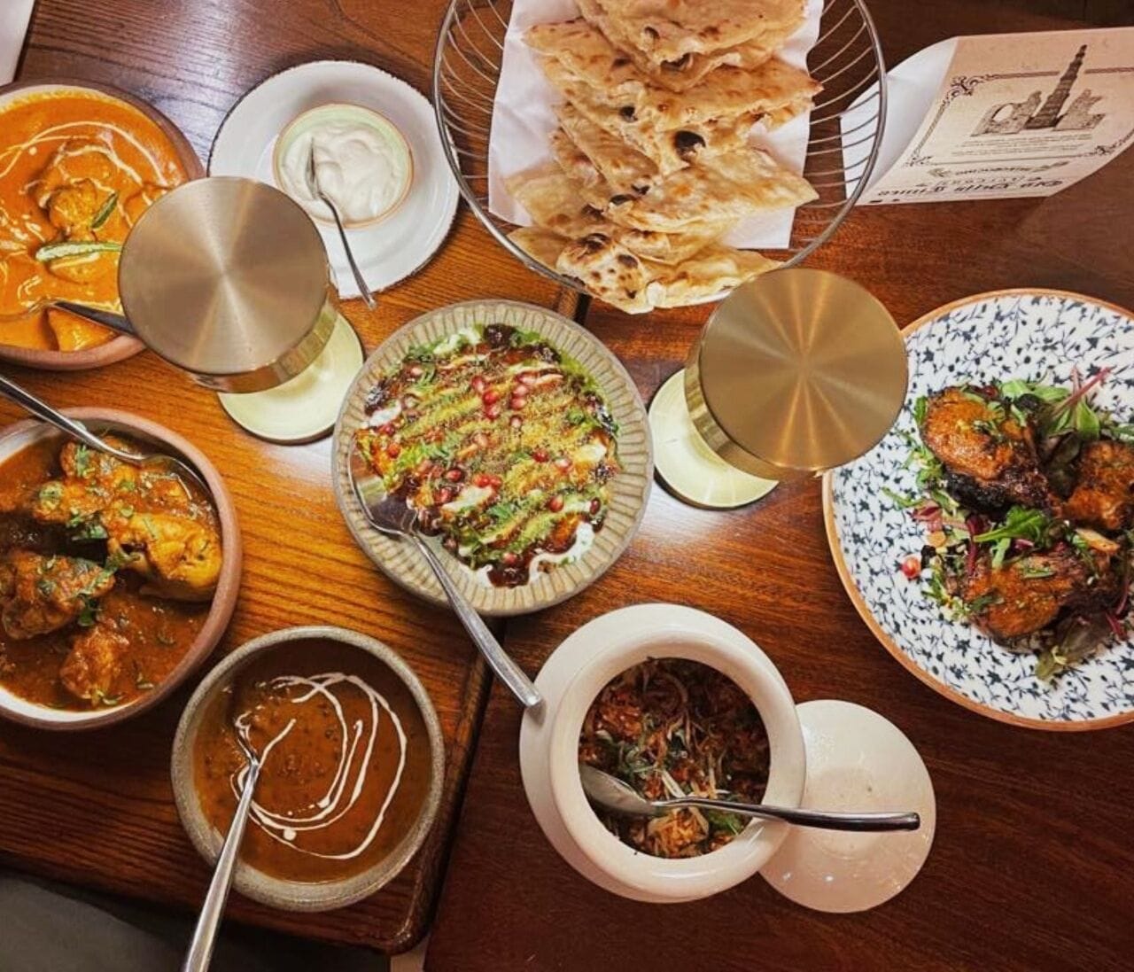 Una variedad de platos sobre una mesa de madera, como curry, pan naan y una ensalada.