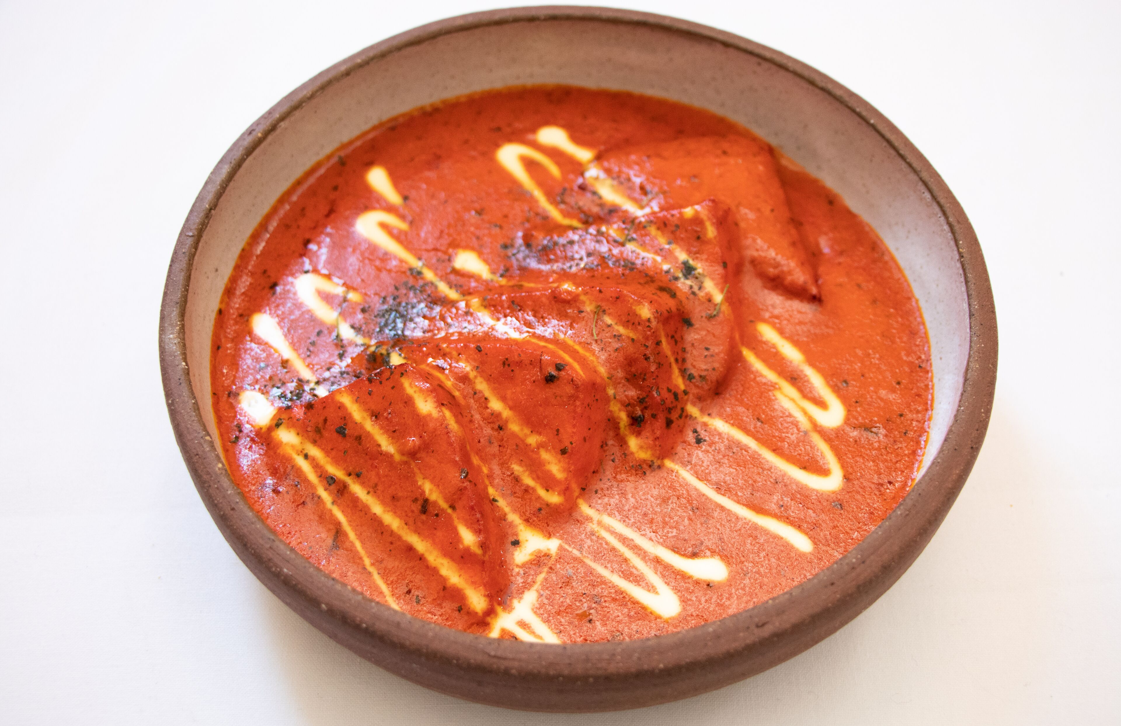 A bowl of red curry with white sauce drizzled on top.