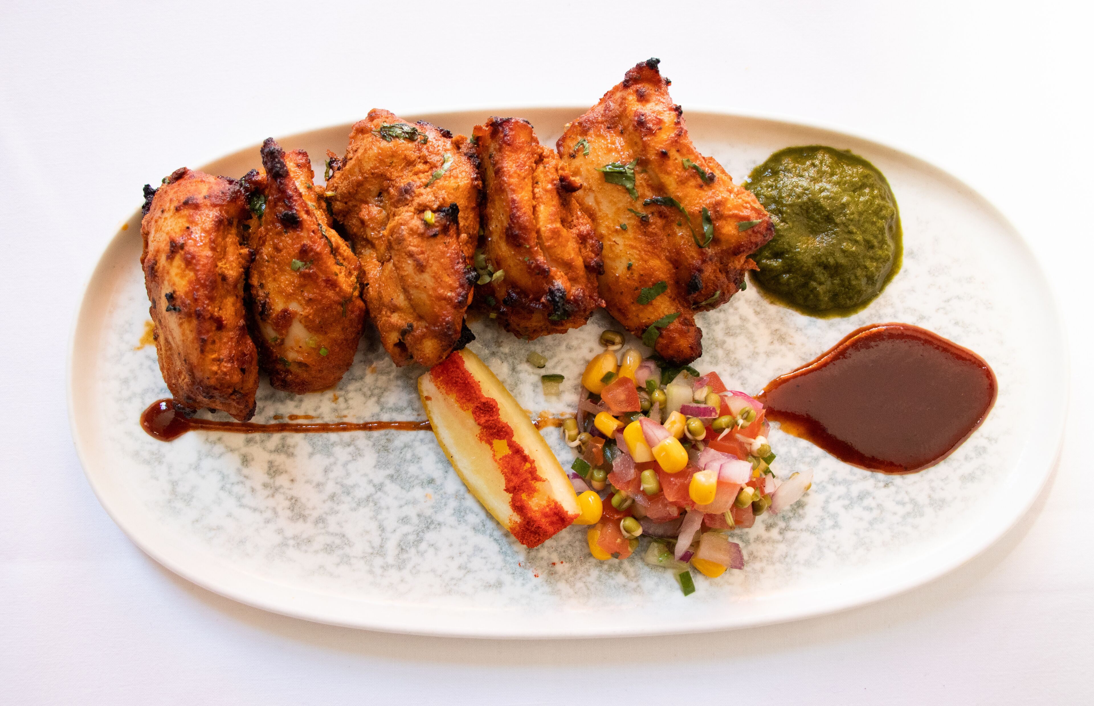 A plate with grilled chicken, a green sauce, a diced vegetable mix, and a dark sauce.