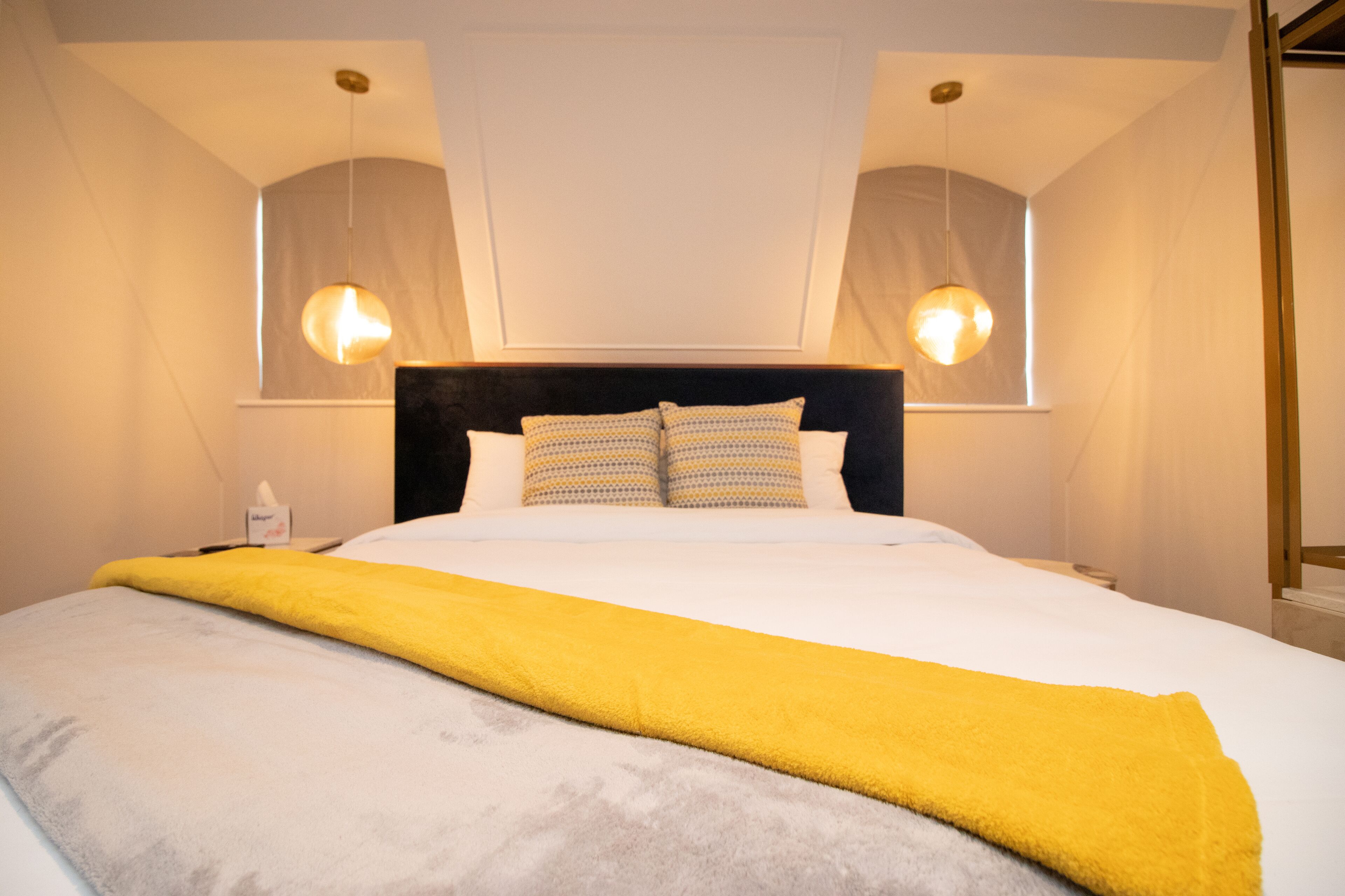 Une chambre d’hôtel avec un grand lit, une tête de lit noire et deux lampes suspendues.