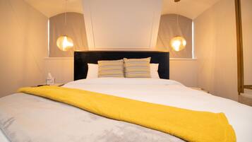 Une chambre d’hôtel avec un grand lit, une tête de lit noire et deux lampes suspendues.