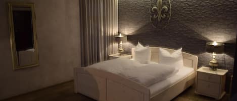 Un dormitorio con una cama grande, dos mesitas de noche con lámparas, un espejo y una pared de piedra decorativa.