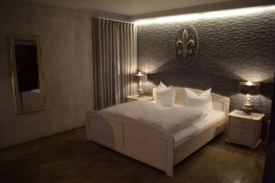A bedroom with a large bed, two bedside tables with lamps, a mirror, and a stone accent wall.