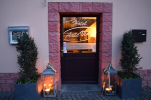 A hotel entrance with a dark door, a sign reading "Hotel Ante Vita," and two lit lanterns on either side.