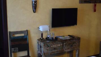 A room with a wooden nightstand, a white lamp, a flat-screen TV, and a chair.