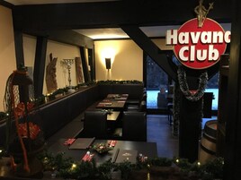 A dining area with a long table set for a meal, a sign reading "Havanc Club", and a view of a snowy landscape through large windows.