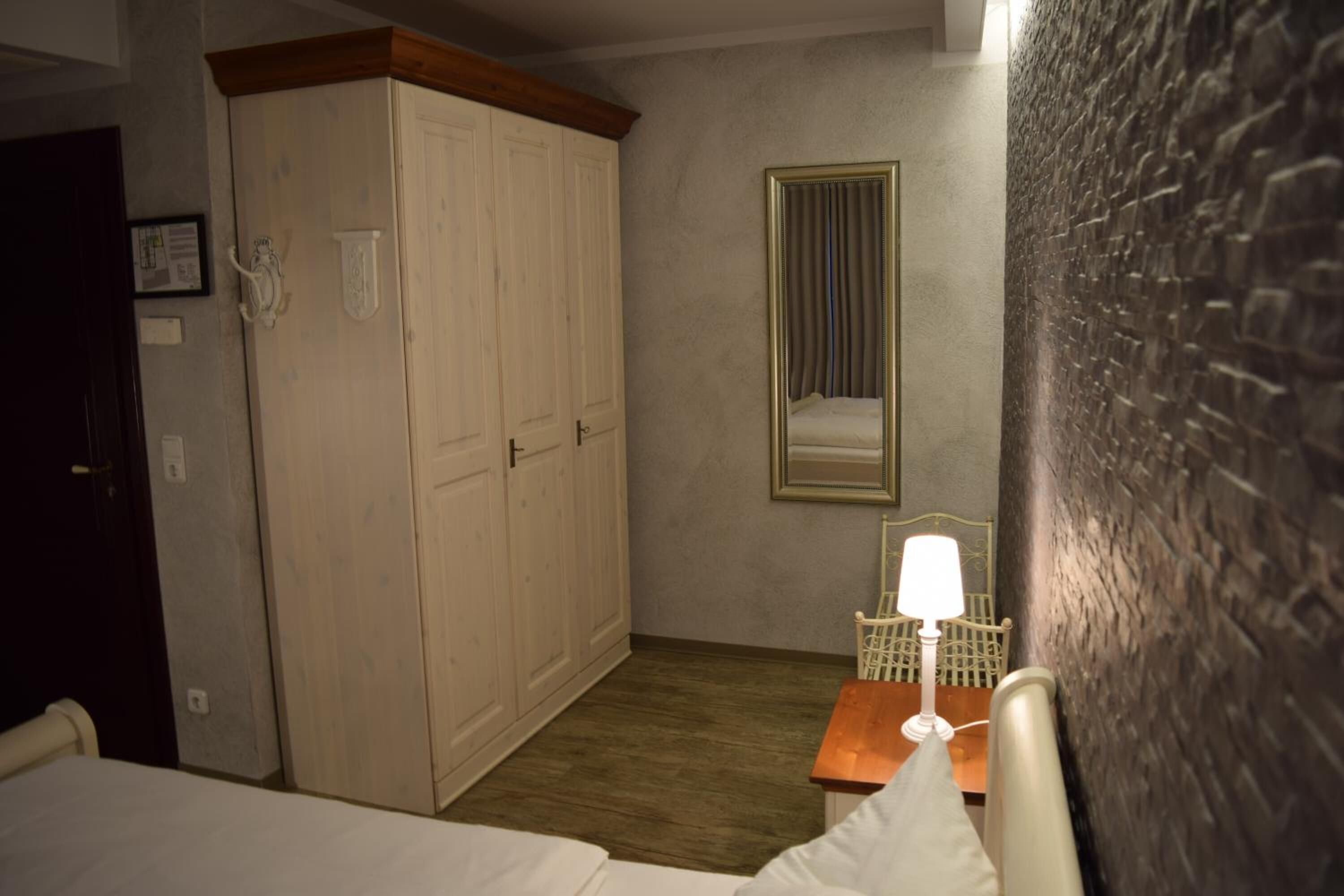 Un dormitorio con cama, armario de madera, mesita de noche con lámpara y espejo en la pared.