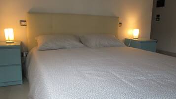 A bed with a patterned bedspread, two bedside tables with lamps, and a plain wall.