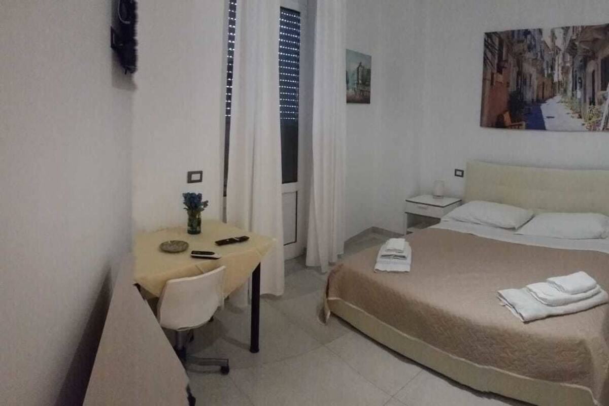 A hotel room with a bed, a desk, a chair, and a painting on the wall.