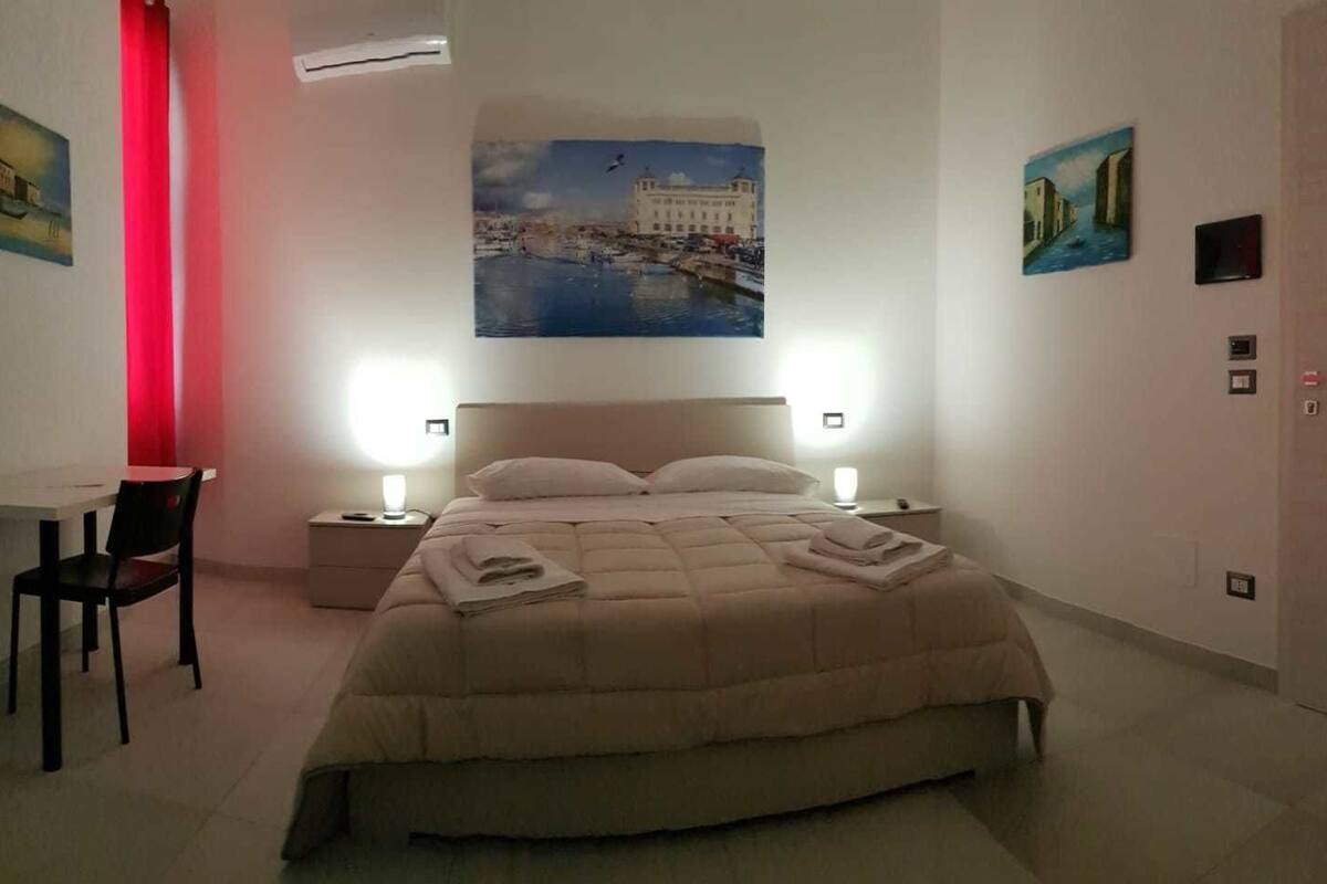 A hotel room with a bed, two bedside tables, a chair, a desk, and artwork on the walls.