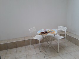 Un balcón pequeño y cerrado, con suelo de baldosas blancas y sillas de metal blanco alrededor de una mesa pequeña con un mantel individual.