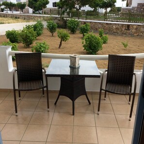 A balcony with two wicker chairs and a table, overlooking a garden with small trees and a stone wall. - Mare Monte (Naxos)