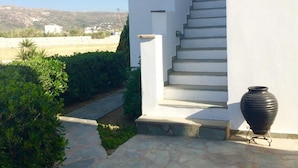 Ein weißes Gebäude mit einer Treppe, die zu einer Tür führt, umgeben von Grünpflanzen und blauem Himmel.