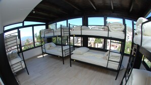 A bunk bed room with a city view, wooden floors, and a high ceiling.