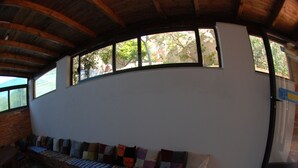 A curved bench with colorful cushions against a white wall, under a wooden ceiling with windows.